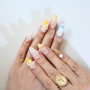 Elegant nude press-on nails with yellow floral design and gemstone pearls