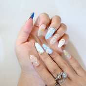 Ocean-inspired press-on nails with gold shell charms, blue gradients, and daisy flowers