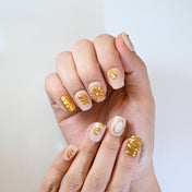 Elegant nude press-on nails featuring golden flowers and abstract 3D swirls