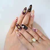 Elegant press-on nails with burgundy floral patterns, gold rose charms, and glossy black details