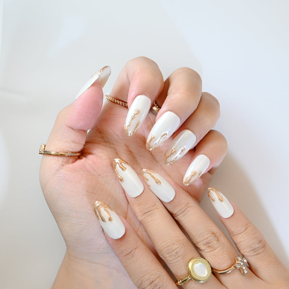 Pearl white press-on nails with gold lava-inspired texture and almond shape