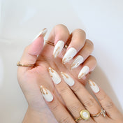 Pearl white press-on nails with gold lava-inspired texture and almond shape