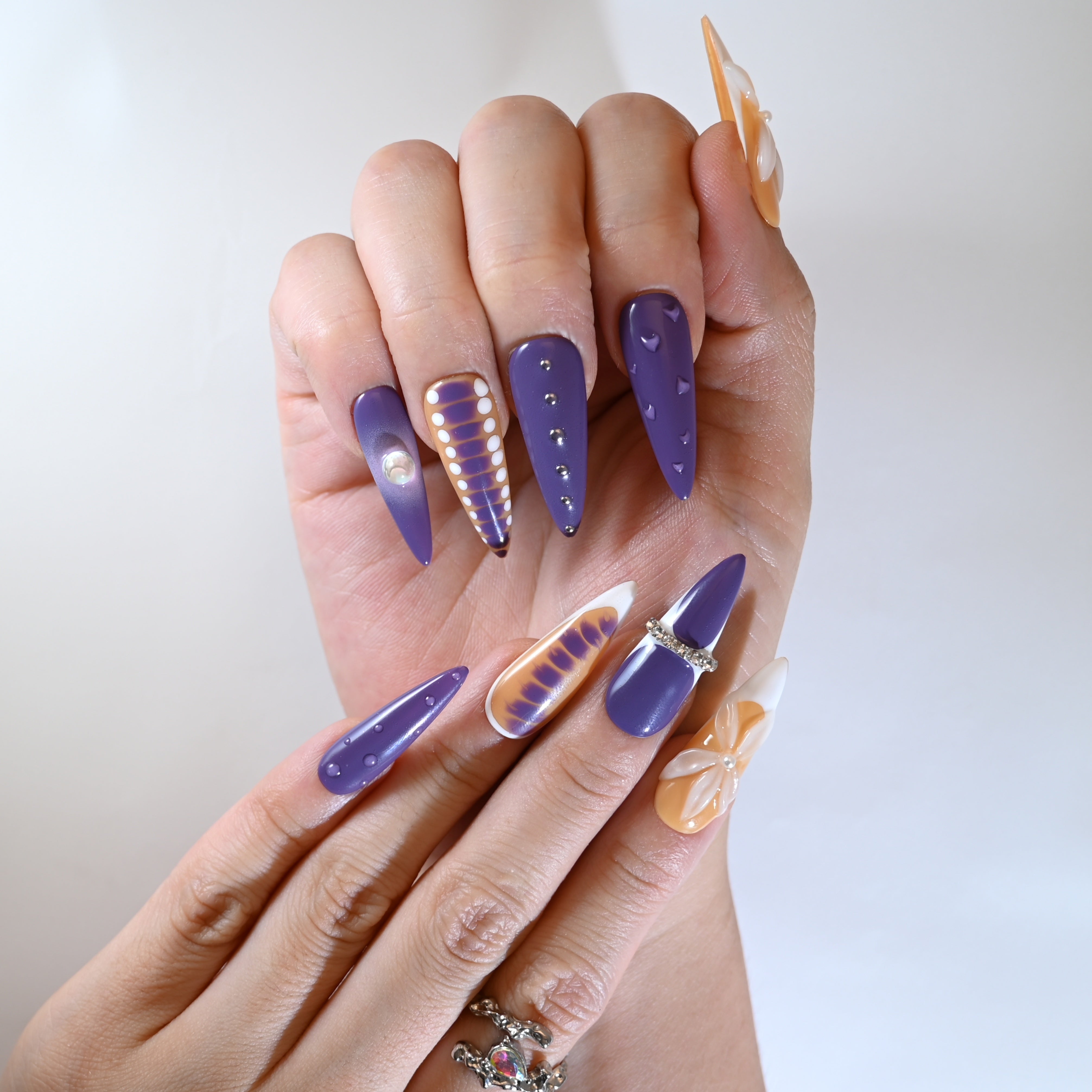 Color-block orange and purple stiletto nails with heart charms and 3D petals