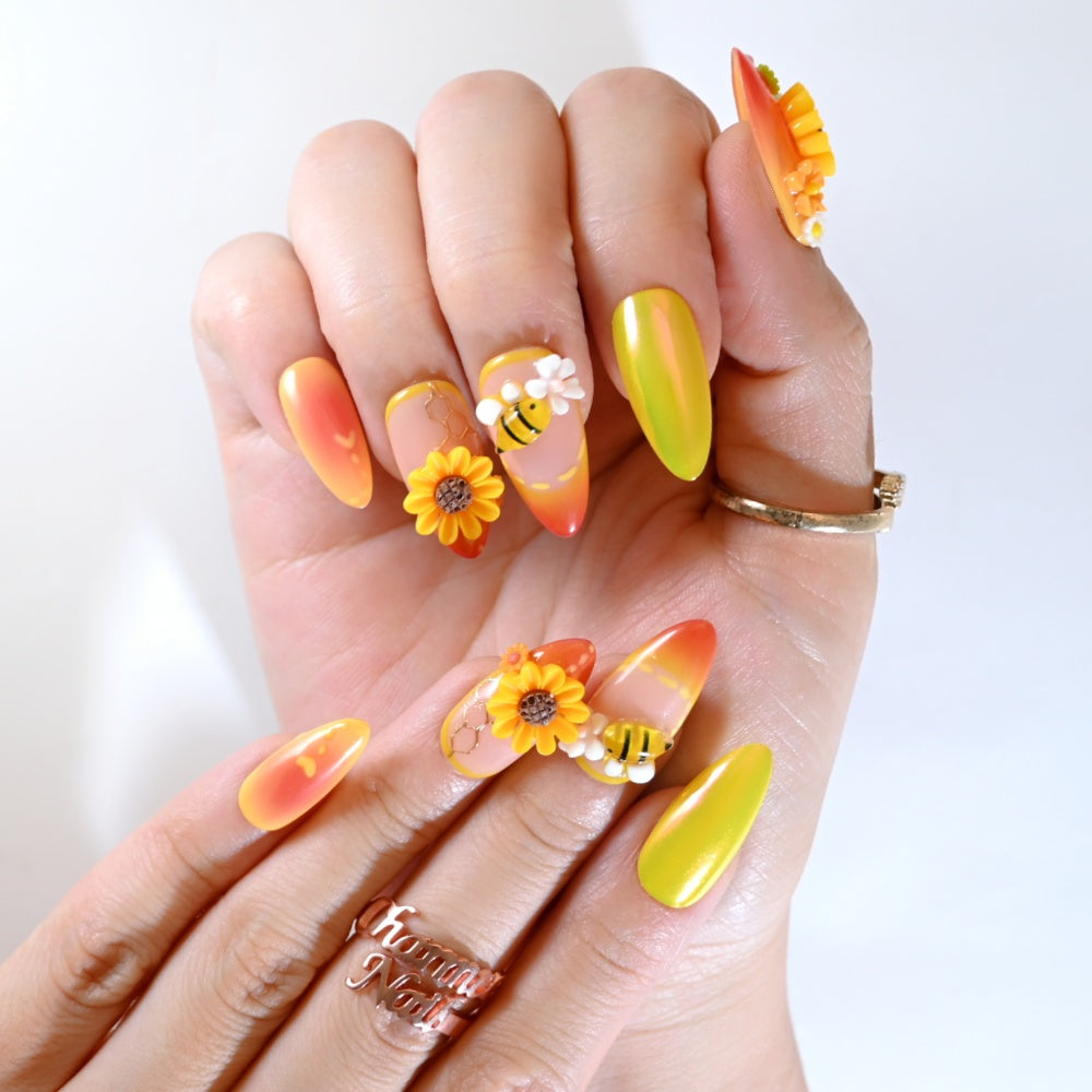 Vibrant 3D sunflower nails with bumblebee design, coral ombre tips, and crystal embellishments