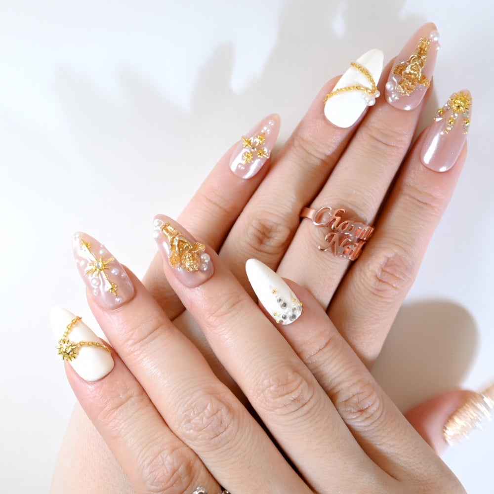 Pink and white press-on nails with golden starburst, pearls, and chain design