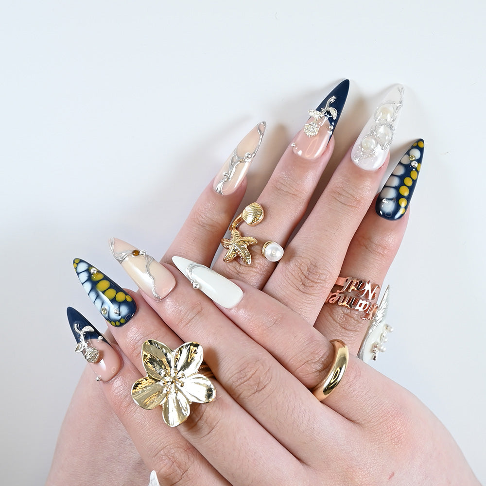 Luxury press-on nails featuring navy gradient, yellow dots, pearl embellishments and floral cross