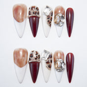 Long stiletto press-on nails with leopard print, burgundy tips, and gemstone accents