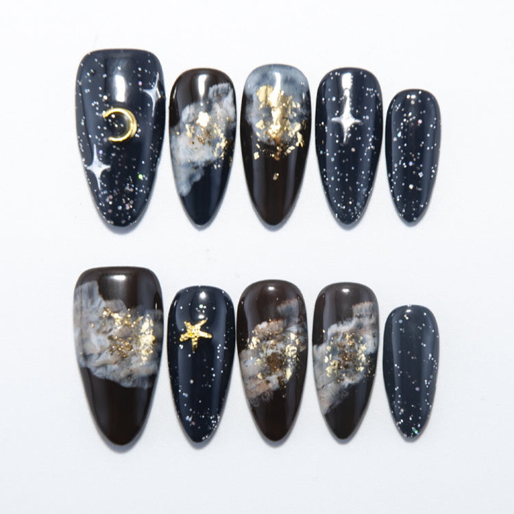 Galaxy press-on nails with black base, gold foil stars, and moon accents