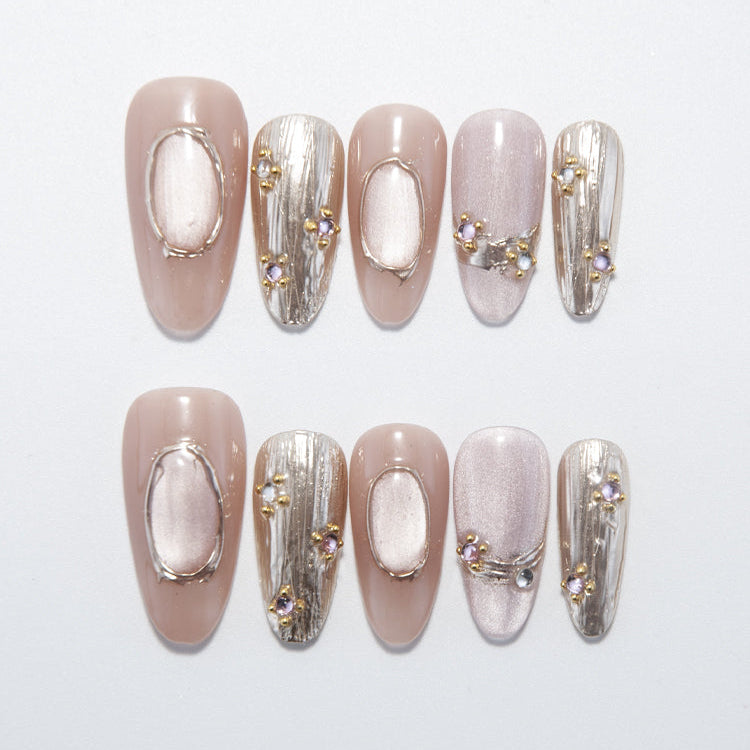 Nude press-on nails with metallic oval accents and gemstone details