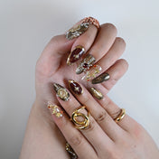 Baroque-inspired press-on nails with deep red polish, gold floral charms, and pearls