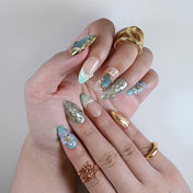 Elegant press-on nails in aqua tones with shimmer finish, gold edges, and flower embellishments